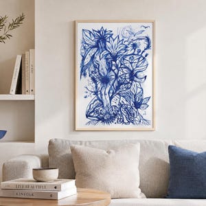 Könnte beinhalten: Ein gerahmter blau-weißer botanischer Kunstdruck hängt über einem Sofa mit neutralfarbenen Kissen. Das Kunstwerk zeigt eine detaillierte Feder- und Tuschzeichnung von Blumen und Blättern. Eine Vase mit Grün und Büchern befindet sich auf einem Regal.