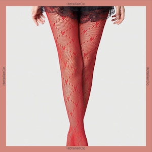 May include: Red fishnet stockings with a heart pattern. The stockings are a vibrant red color and feature a repeating heart design. The image shows the stockings from the mid-thigh down, with a glimpse of black lace at the top.