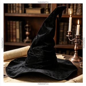 Peut inclure: Un chapeau de sorcière en velours noir avec une calotte haute, pointue et légèrement affaissée, ainsi qu'un large bord souple. Le tissu présente un léger éclat et le chapeau a une apparence structurée mais douce. Le texte HatelierCo est visible.