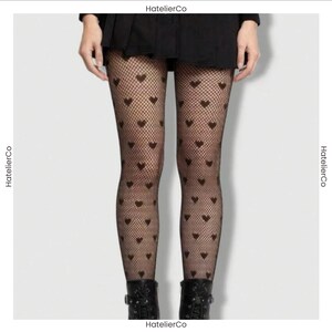 May include: Black fishnet tights featuring a repeating pattern of small, solid black hearts. The hosiery is worn under a black skirt and paired with black boots. The text HatelierCo is visible on the borders of the image frame.