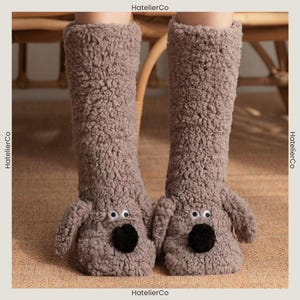 May include: Knee-high, taupe-coloured dog-shaped socks. The socks have a plush, textured appearance with a black nose, white eyes, and small ear details. Designed to cover the feet and lower legs.