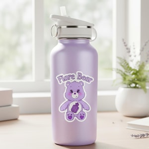 Puede incluir: Una botella de agua de color lila con tapa y pajita blancas. Una pegatina de un oso de dibujos animados morado con el texto "Flare Bear" está en la botella. La botella está sobre una superficie de madera cerca de una ventana.