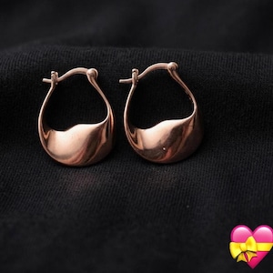 May include: A pair of rose gold hoop earrings with a smooth, curved, and teardrop-shaped design. The earrings feature a polished metallic finish and a hinged closure mechanism at the top, showcasing a continuous, flowing silhouette in a warm tone.