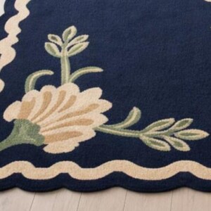 May include: A navy blue rug with a scalloped edge and floral design. The rug features a cream-colored border and cream, green, and tan floral accents. The floral pattern includes stylized flowers and leaves.