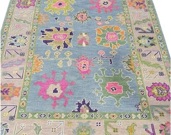 Könnte beinhalten: Rechteckiger Teppich mit hellblauem Mittelfeld. Der Teppich hat ein Blumenmuster in Rosa, Grün, Orange und Lila. Der Rand ist eine Mischung aus Beige, Grün und floralen Motiven. Der Teppich ist für die Inneneinrichtung konzipiert.