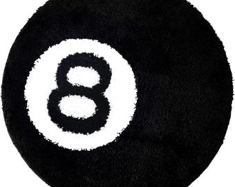 May include: A round, black bath mat with a white circle and the number 8 in the center. The mat has a plush, textured surface, resembling a pool ball.