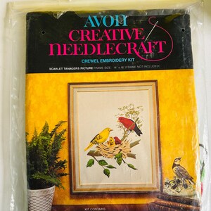 May include: An Avon Creative Needlecraft crewel embroidery kit in a clear plastic bag. The packaging features a yellow background with a picture of a scarlet tanager bird family in a nest. It includes text stating a 35.5 cm by 45.7 cm frame size.