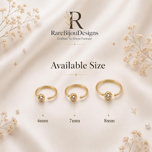 May include: Three gold-colored nose rings with a clear gem in the center, displayed on a cream-colored surface. Sizes are 6mm, 7mm, and 8mm. The brand name "RareBijouDesigns" is visible.