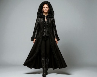 May include: A long, black coat with a faux fur-lined hood and trim. The coat features a fitted bodice with a lace-up detail and flared skirt. The sleeves have fur cuffs, and the model is wearing black pants and boots.