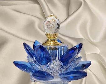 May include: A decorative glass perfume bottle shaped like a lotus flower with deep blue crystal petals and a clear crystal base. The centre features a gold-toned metal neck topped with a faceted, diamond-shaped clear crystal stopper.