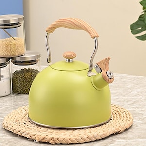 May include: A light green stovetop kettle with a wooden handle and spout detail. The kettle sits on a woven placemat. Glass jars with lids are in the background.