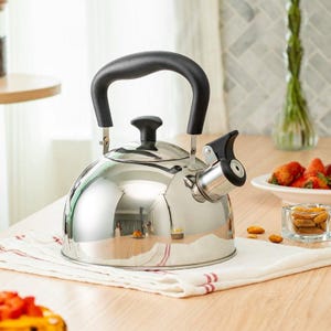 以下が含まれることがあります： 黒いハンドルと注ぎ口が付いた、光沢のあるステンレス製のティーケトル。 ケトルは、木製のテーブルの上の白と赤のストライプの布の上にあります。 イチゴとアーモンドが背景にあります。