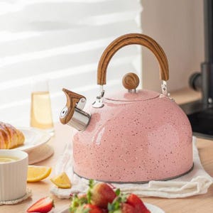 May include: A pink speckled tea kettle with a wooden handle and spout. The kettle sits on a white cloth, with a plate of strawberries and a cup of tea in the foreground. The handle is approximately 6 inches (15 cm) tall.