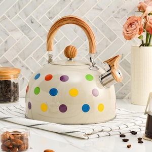 Puede incluir: Hervidor de cocina crema con un patrón de lunares en varios colores. El hervidor tiene un asa de madera y un pomo de madera en la tapa. La boquilla y el mango del silbato también tienen detalles de madera. Un elegante accesorio de cocina.