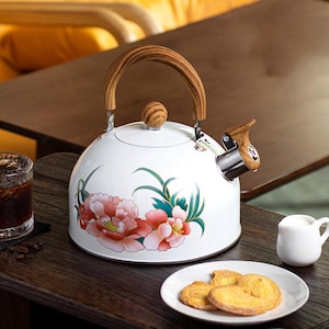 May include: White enamel tea kettle with a floral design in pink and red. The kettle has a wooden handle and spout lever. A small white creamer pitcher and a plate of cookies are on the table.