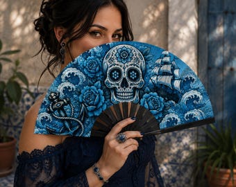 May include: A folding hand fan featuring a detailed blue and white illustration of a skull, roses, a sailing ship, and an anchor. The fan has dark wooden ribs and a semi-circular shape, displaying a nautical and floral theme in shades of blue.