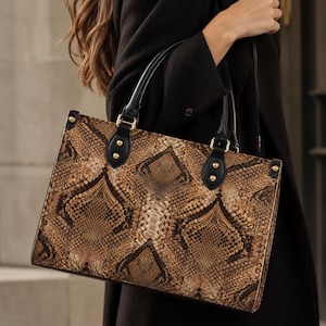 May include: A structured rectangular handbag featuring a brown and black snakeskin pattern. The bag includes two black top handles attached with gold-toned metal hardware and rivets. The design showcases a repeating diamond scale texture.