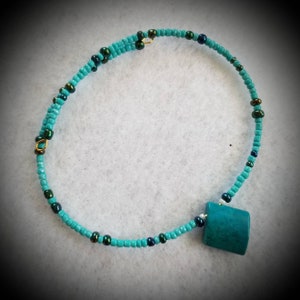 May include: A turquoise and green beaded necklace with a turquoise pendant. The necklace is made of small beads and has a gold clasp.