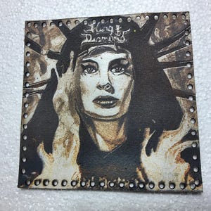 May include: Square, sepia-toned artwork featuring a woman's portrait with the text "King Diamond" on a headpiece. The image has a distressed, vintage aesthetic, with flames depicted on either side of the face. The edges are perforated with small holes.