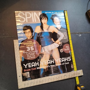 May include: A vintage SPIN magazine cover featuring the band Yeah Yeah Yeahs. The cover has a blue and white color scheme with the text "YEAH YEAH YEAH'S" and "Break Out! Meet Rock's New Queen of Cool". The magazine is measured with a ruler.