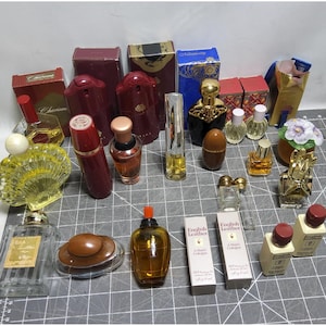 Pode incluir: Uma coleção de frascos de perfume e colónia vintage, com várias formas, tamanhos e cores. O sortido inclui frascos com desenhos ornamentados, caixas e a colónia "English Leather". Os frascos estão dispostos numa superfície cinzenta.