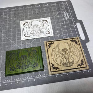 May include: Three wooden plaques with dragon and bat designs. One is white, one is stained green, and the other is natural wood. The dragon is centered with outstretched wings. Bats are in the corners of the natural wood plaque.