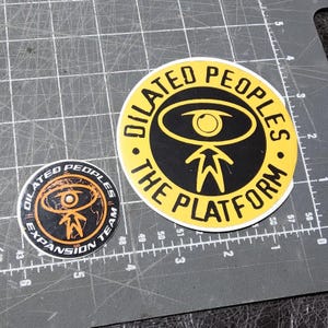 May include: Two circular stickers with the text "DILATED PEOPLES" and "THE PLATFORM". One sticker is black and yellow, the other is black, orange, and white, with the text "EXPANSION TEAM".