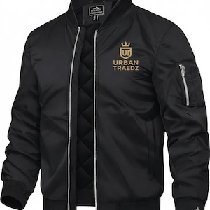 Puede incluir: Chaqueta bomber negra con forro acolchado y logotipo dorado "URBAN TRAEDZ". Tiene cierre de cremallera, puños de canalé y bolsillo en la manga. Una chaqueta clásica y versátil.