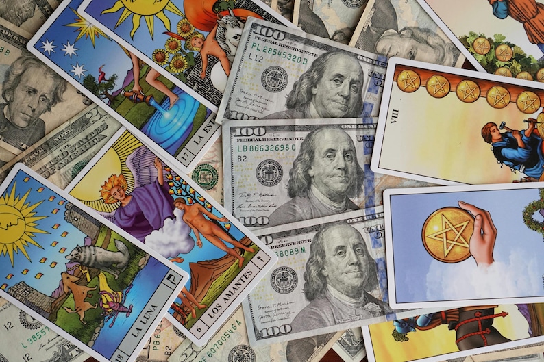 Puede incluir: Una colecci&oacute;n de cartas del tarot con ilustraciones coloridas, incluyendo El Sol, Los Amantes y La Luna, se exhiben junto a varios billetes de cien d&oacute;lares. Las cartas presentan varias figuras y s&iacute;mbolos.