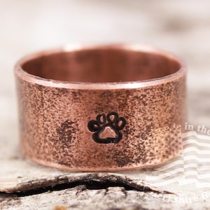 May include: A copper ring with a distressed finish and a black paw print design. The ring is made in the USA.