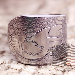 May include: A silver ring with a detailed design of a wolf's head. The ring is textured and has a hammered finish. The text "Handmade in the USA by Berkshire Bros." is visible on the ring.