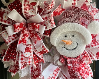 Könnte beinhalten: Ein festlicher Weihnachtskranz mit Schneemann- und Schneeflocken-Design. Der Kranz ist mit rot-weißen Bändern, Mesh und einer Schneemannfigur mit Karottennase verziert. Ideal für festliche Weihnachtsdekorationen.