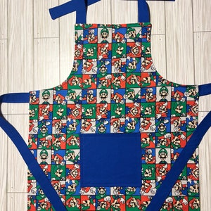 May include: A blue and white apron with a repeating pattern of Mario and Luigi characters. The apron has a large blue pocket on the front.