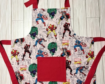 Könnte beinhalten: Rote und weiße Küchenschürze mit einer Tasche. Die Schürze zeigt ein Muster mit Marvel Comics-Superhelden, darunter Captain America, Iron Man, Hulk und Spider-Man. Der Text "MARVEL COMICS" erscheint auf der Schürze.