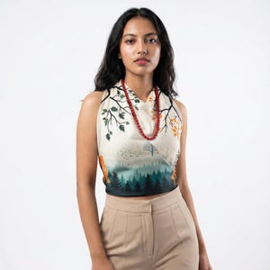 Può includere: Top senza maniche con stampa di scena di foresta nei toni del verde, arancione e beige. Il top presenta un design paesaggistico con alberi e una foresta. Una collana di perline rosse viene indossata con il top.