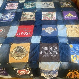 May include: A patchwork quilt constructed from various graphic t-shirts and denim fabric squares. The quilt features diverse prints including text like 'A BOSS', 'Hard Rock', 'HUNTINGTON POSTAL SERVICE', and 'adidas', joined by frayed denim seams.