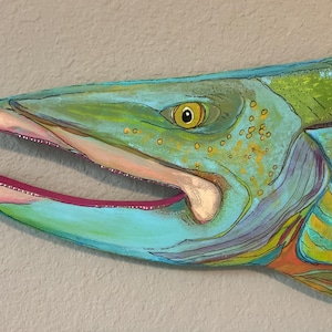 May include: A colorful painted wall art piece depicting the head of a fish with an open mouth. The artwork features vibrant shades of turquoise, green, and yellow, with a bright pink interior of the mouth and a detailed yellow eye with a black pupil.