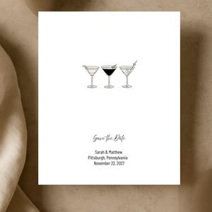 May include: White square card with three martini glasses in a row. The glasses are filled with different colored liquids and garnished. The text "Save the Date" is written in cursive, along with names, city, state, and date.