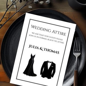Op de afbeelding: Een huwelijksuitnodiging met de tekst "WEDDING ATTIRE" en "JULIA & THOMAS". De uitnodiging bevat illustraties van een zwarte jurk en een smoking. De uitnodiging ligt op een zwart bord met een vork.