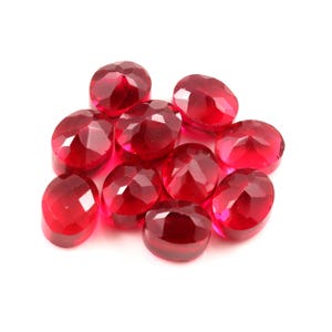Può includere: Un gruppo di gemme rosse, ovali e sfaccettate. Le gemme sono disposte su uno sfondo bianco. Le sfaccettature catturano la luce, creando un effetto scintillante. Adatte per la creazione di gioielli o altri lavori manuali. Misurano circa 1,5 cm.