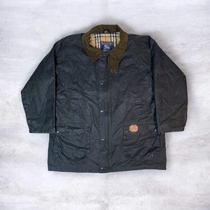 May include: A dark green waxed cotton jacket with a corduroy collar and a plaid lining. The jacket has a button-up front, two front pockets, and a small leather patch. The jacket is laid flat on a light gray surface.