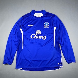 May include: A long-sleeved, royal blue Everton soccer jersey. The jersey features white accents on the sides and a white collar. The Chang logo is prominently displayed on the front, along with the Everton team crest and the Umbro logo.