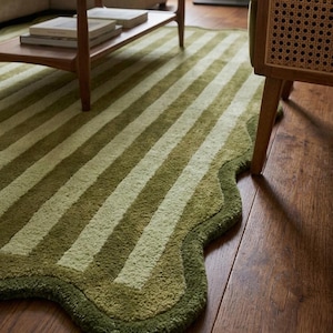 May include: A rectangular area rug featuring a repeating pattern of alternating olive green and light sage green stripes. The rug has a distinctively curved, scalloped edge border in a solid dark olive green, creating a soft, wavy perimeter.