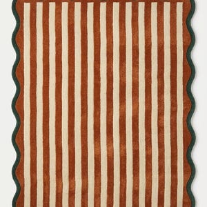 May include: A rectangular rug featuring a pattern of vertical stripes in rust orange and cream. The rug is finished with a dark green scalloped border that follows the wavy edge of the textile, creating a distinct contrast against the striped center.