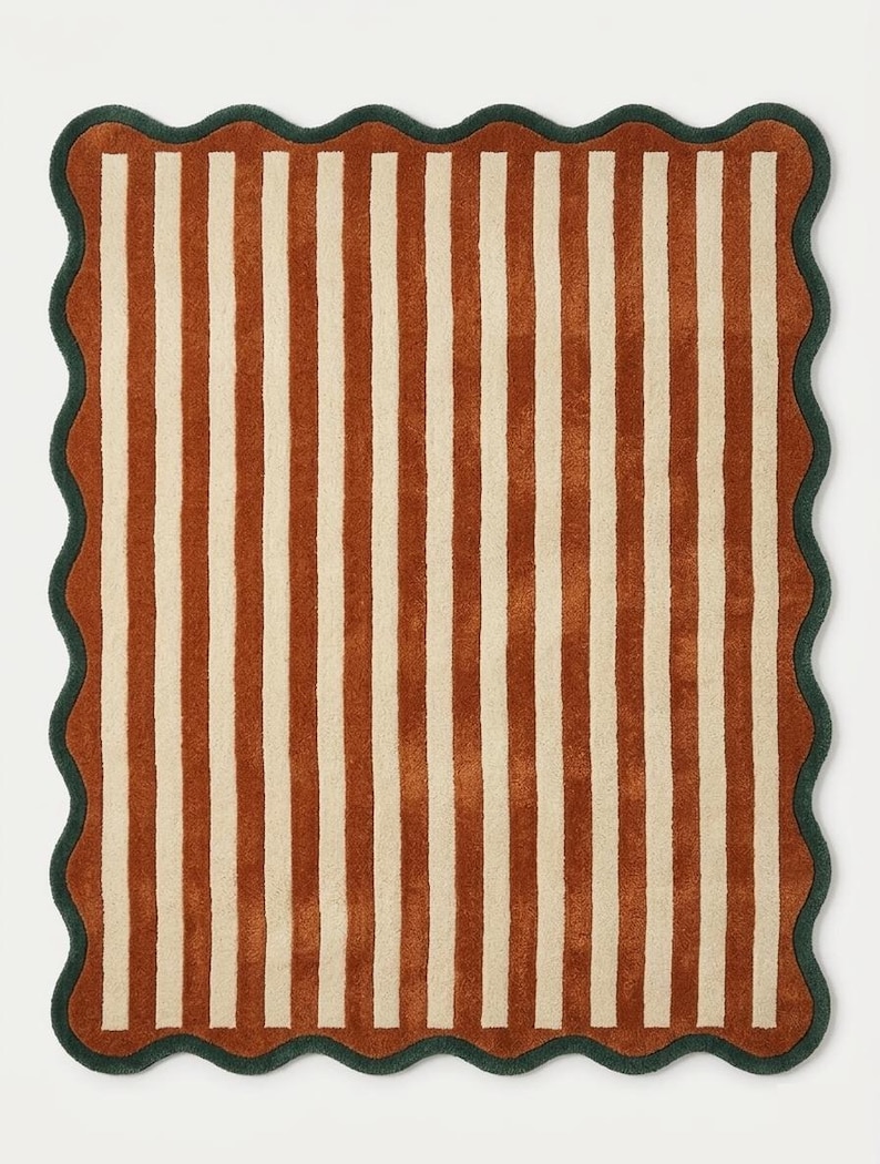 May include: A rectangular rug featuring a pattern of vertical stripes in rust orange and cream. The rug is finished with a dark green scalloped border that follows the wavy edge of the textile, creating a distinct contrast against the striped center.