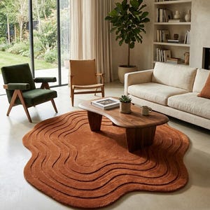 May include: An irregular, organic-shaped area rug in a deep terracotta orange color. The rug features a textured surface with concentric, wavy, raised lines that follow the perimeter of the shape, creating a layered, topographical appearance.