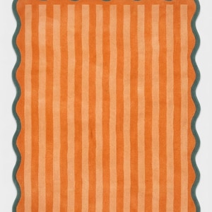 May include: A rectangular rug featuring vertical stripes in alternating shades of bright orange and light peach. The rug is finished with a dark teal scalloped edge that follows the wavy contour of the entire perimeter of the piece.