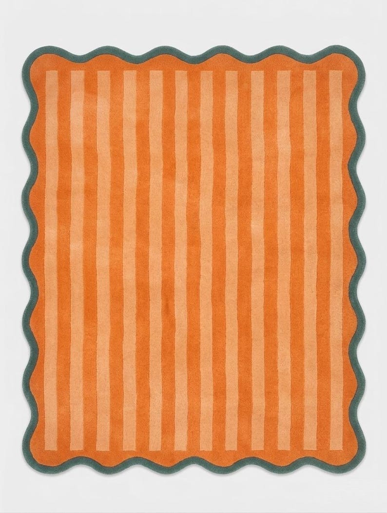 May include: A rectangular rug featuring vertical stripes in alternating shades of bright orange and light peach. The rug is finished with a dark teal scalloped edge that follows the wavy contour of the entire perimeter of the piece.