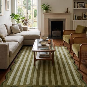 May include: A rectangular area rug featuring a scalloped edge and a vertical striped pattern in alternating shades of olive green and cream. The rug is constructed with a textured pile and is positioned on a wooden floor beneath a coffee table.