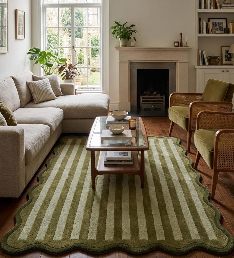 May include: A rectangular area rug featuring a scalloped edge and a vertical striped pattern in alternating shades of olive green and cream. The rug is constructed with a textured pile and is positioned on a wooden floor beneath a coffee table.